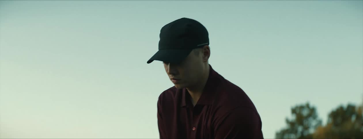Golf player on a field at morning places a ball over a tee and hits it with a club