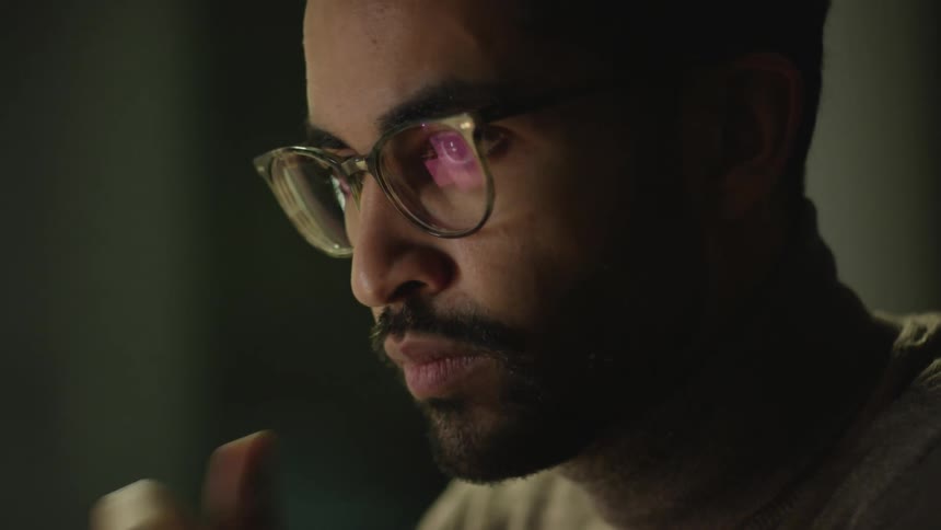 Man with facial hair and glasses looks down as he works on something below his gaze