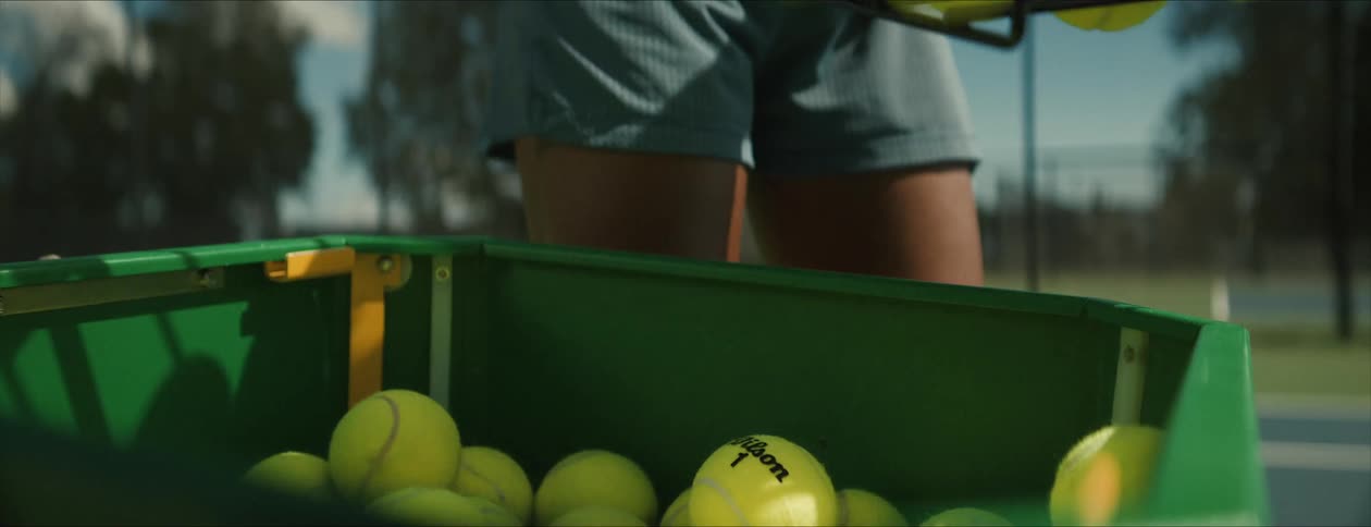 Tennis player empties a basket full of balls into a container on the court