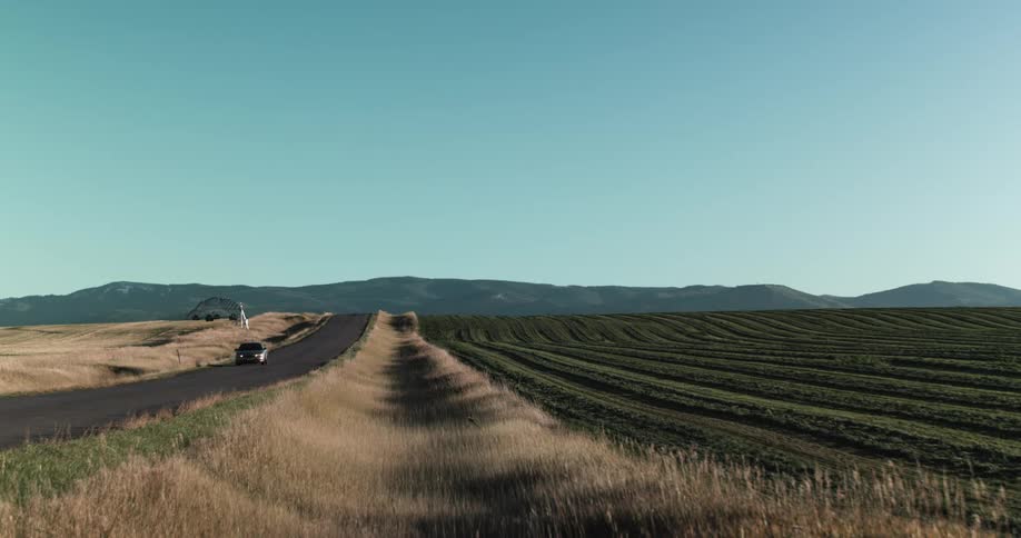A car travels along a road through the countryside under a clear sky