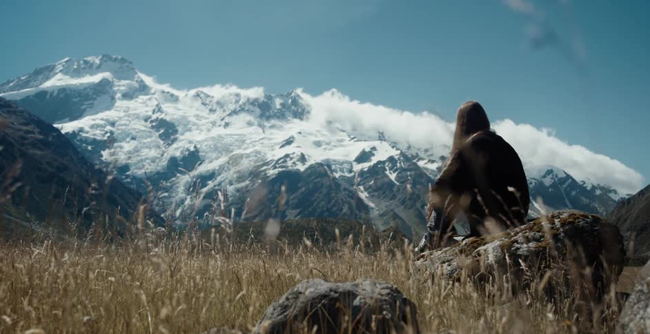 Female sitting on a rock overlooking snow capped mountain peaks
