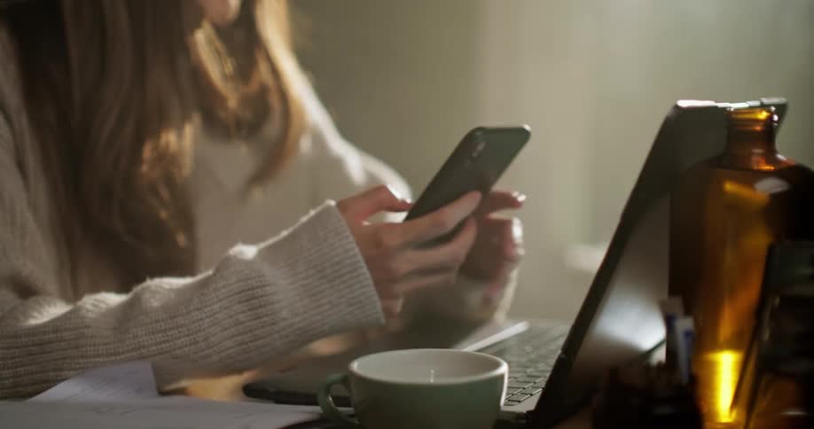 Young woman texting on smartphone at sunrise in cafe