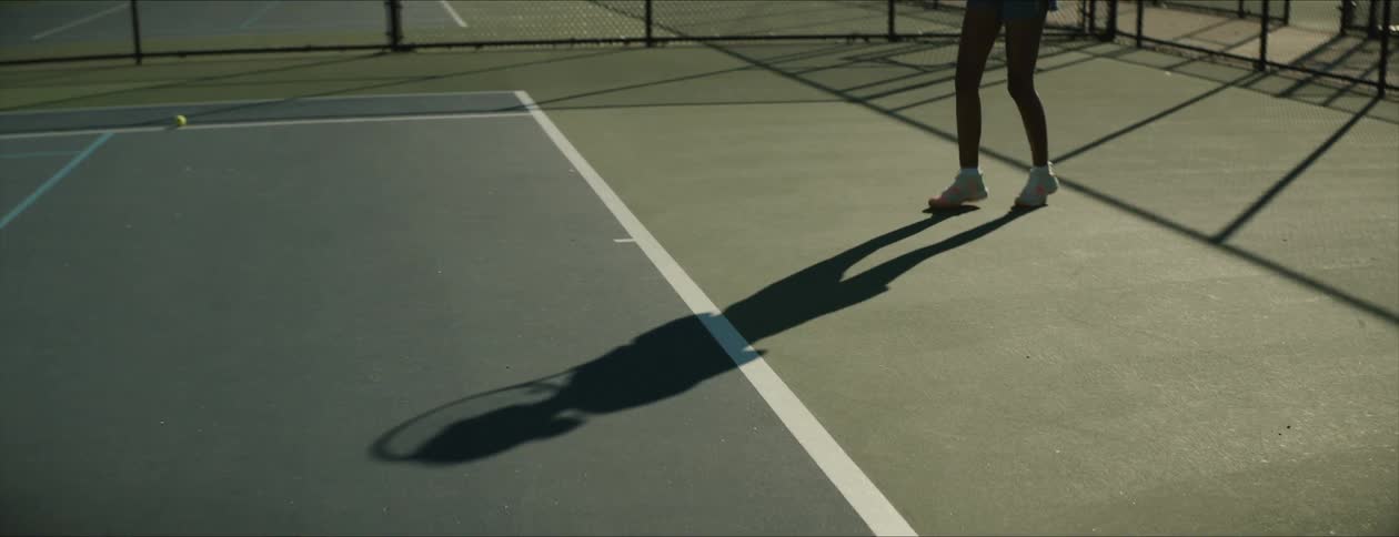 Shadow of a female tennis player playing on a court at morning