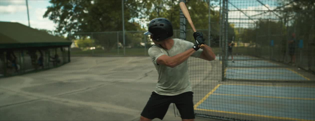 Man wearing a helmet swings a bat on a baseball practice booth