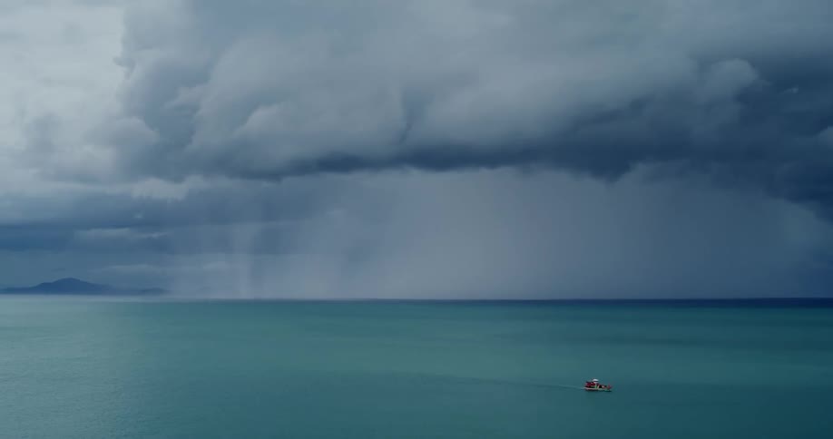 A boat travels across the ocean under thick clouds during the day