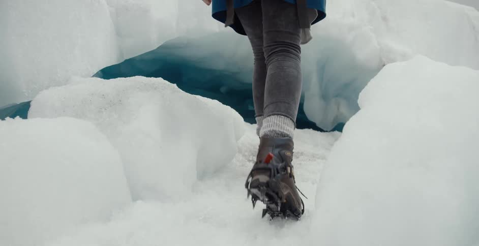 Person wearing cleats walks across ice toward blue interior of ice cave