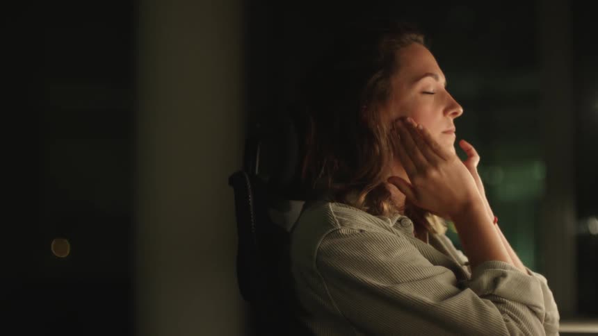 Woman working at the office late at night reclines on her chair tiredly