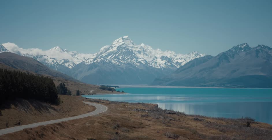 Road near a lake next to the snow covered peaks of a mountain range
