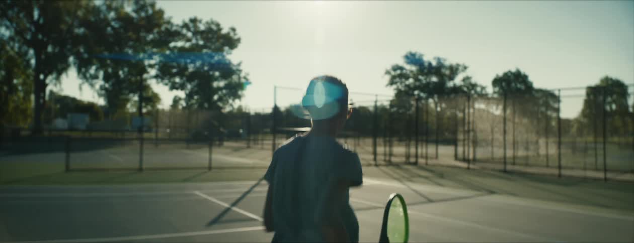 A woman walks over to her spot on a tennis court holding a tennis racket