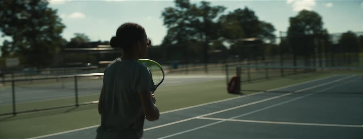 Young woman practices tennis alone on a court at morning