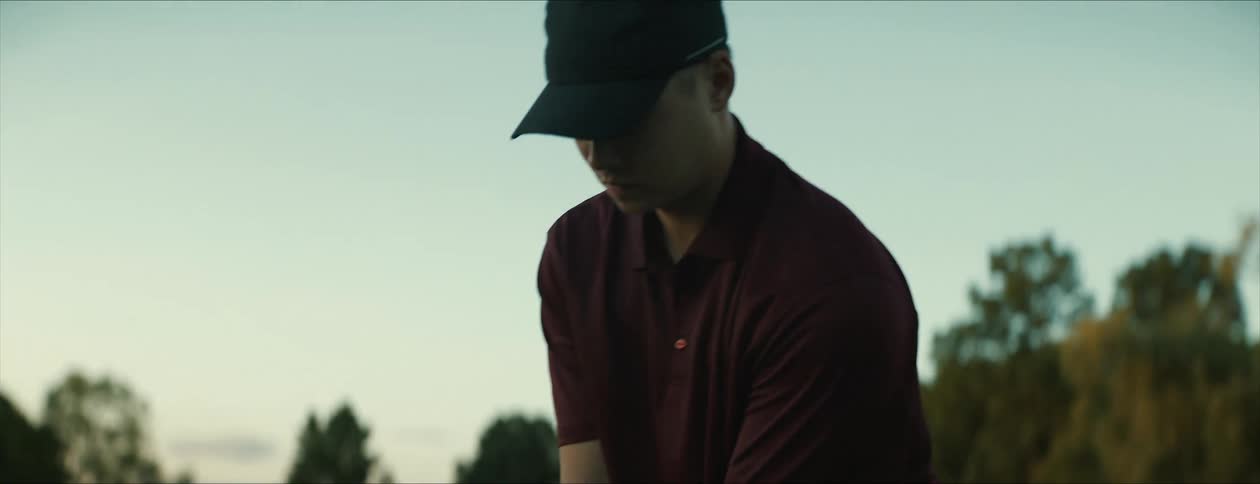 Golf player on a field at morning places a ball over a tee and hits it with a club