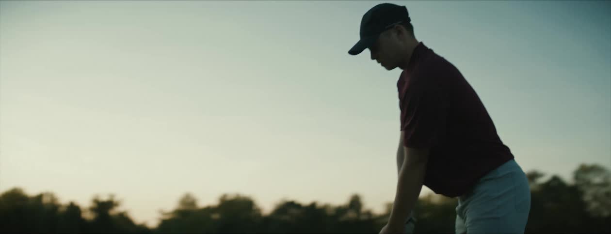 A man hits a golf ball on a driving range in the evening