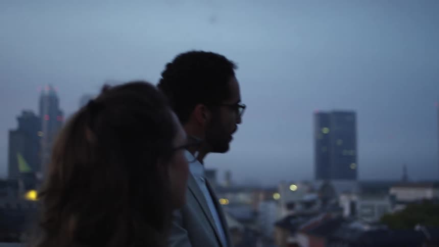 Man and woman walk and talk with hazy city downtown in the background