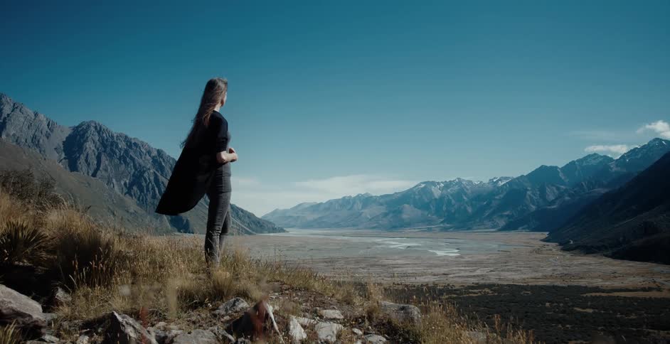 A young woman stands and looks out at a mountain range