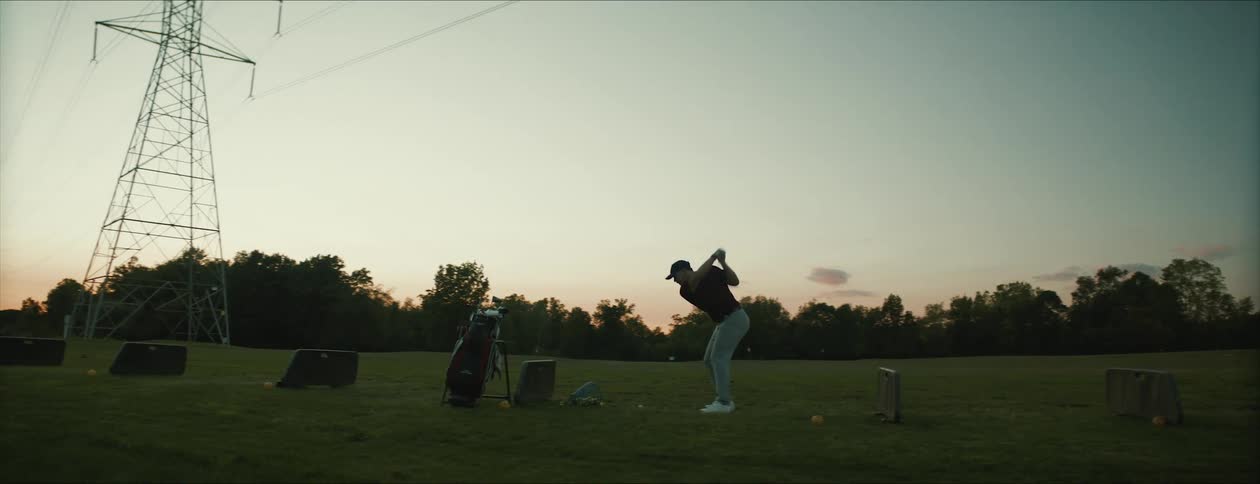 A golfer swings at a golf ball under power lines