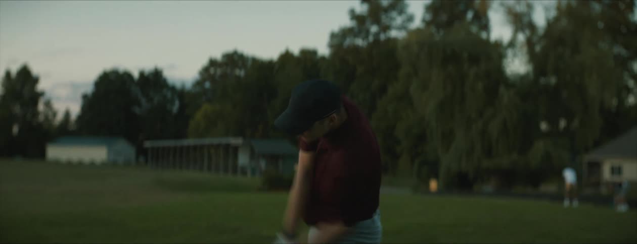 Golfer with cap and club hits ball at golf course