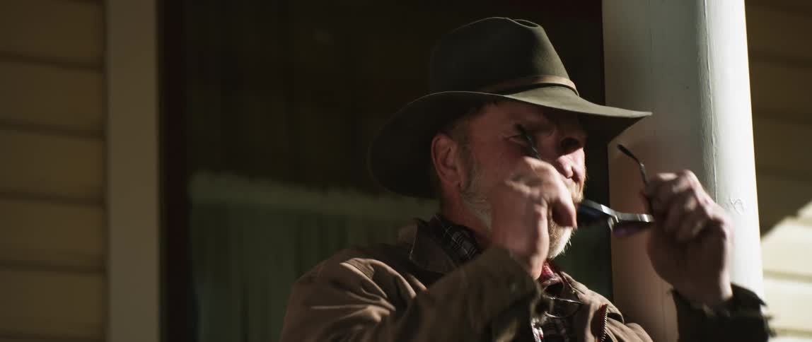 A man wearing a cowboy hat is standing outside a building and puts on his sunglasses