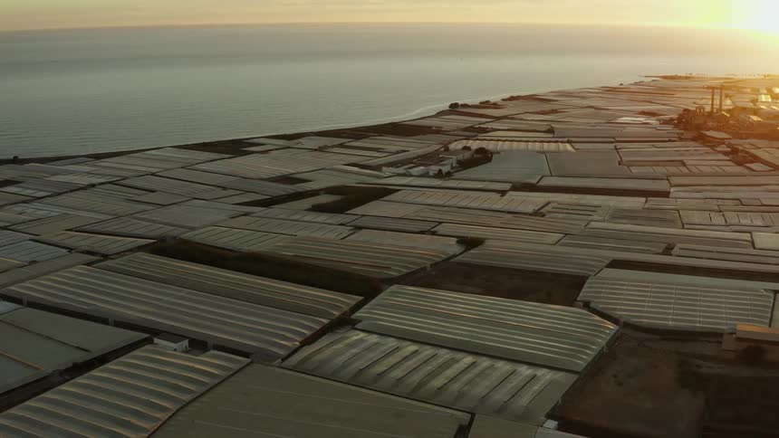 Greenhouse roofs cover a vast area along the coast as sun sets below the horizon