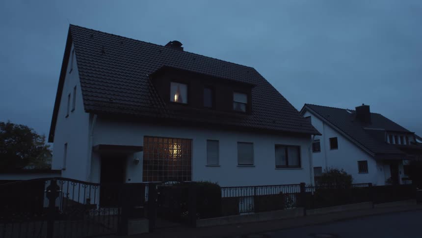 Light comes on in home shining through window under an overcast sky