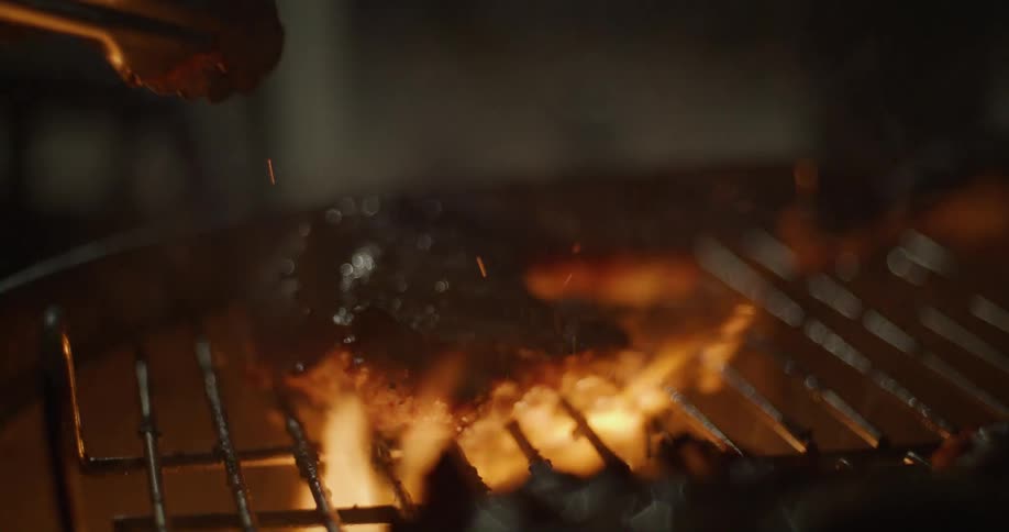 Flipping chicken over the open flames of a grill at night