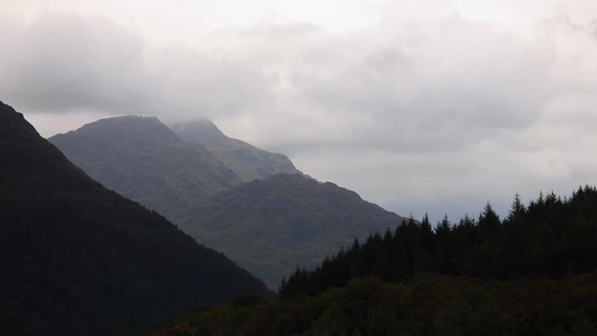 Thick clouds pass over a forested mountain range during the day