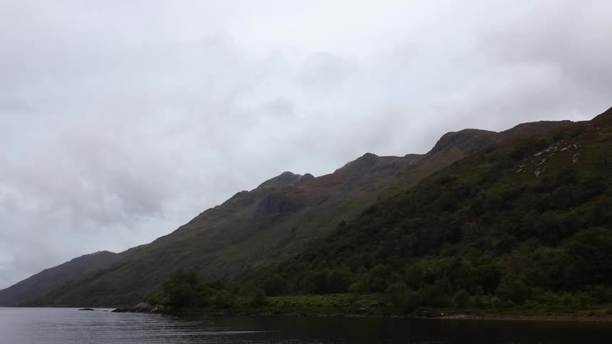 Water laps at a mountainous coastline on a cloudy day