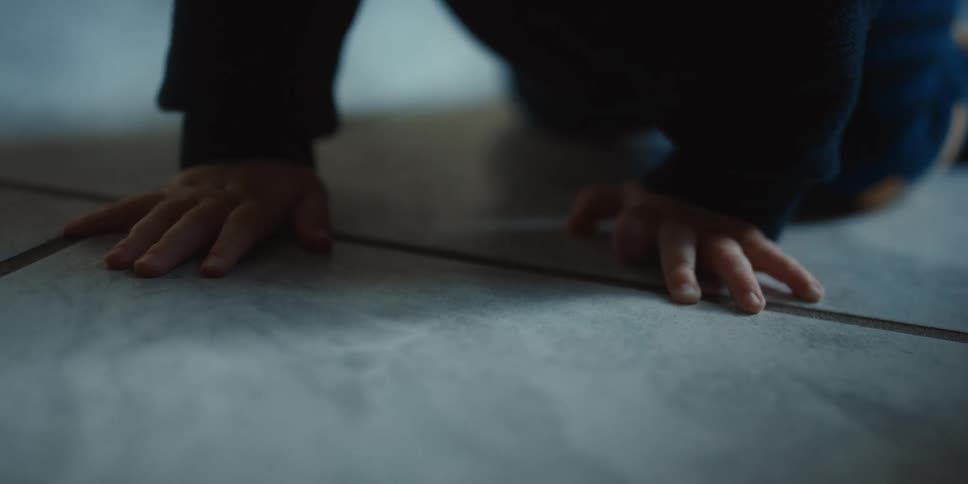 Baby wearing a long sleeved shirt crawls across tiled floor