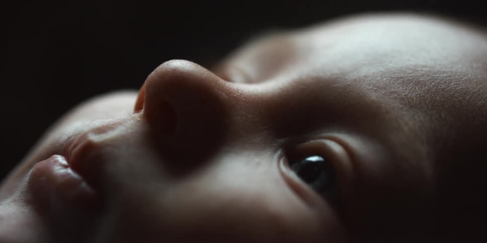 A baby waves its hand in the air while lying down