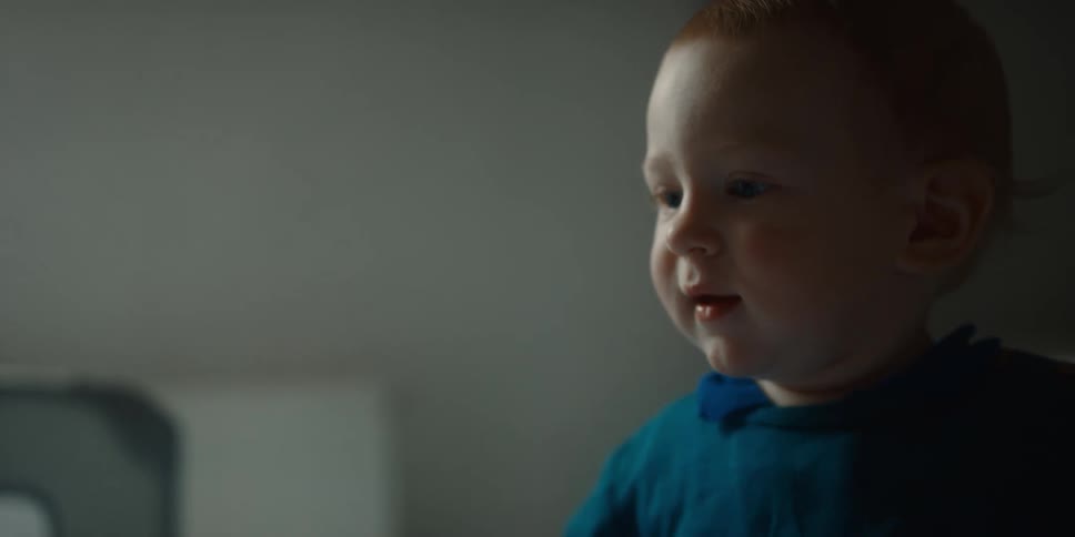 Light shines on the smiling face of a baby standing and waving their arms up and down
