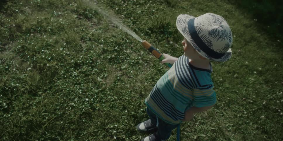 Child stands watering lawn with water hose