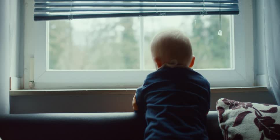 A young baby stands up in his home and reaches for a toy