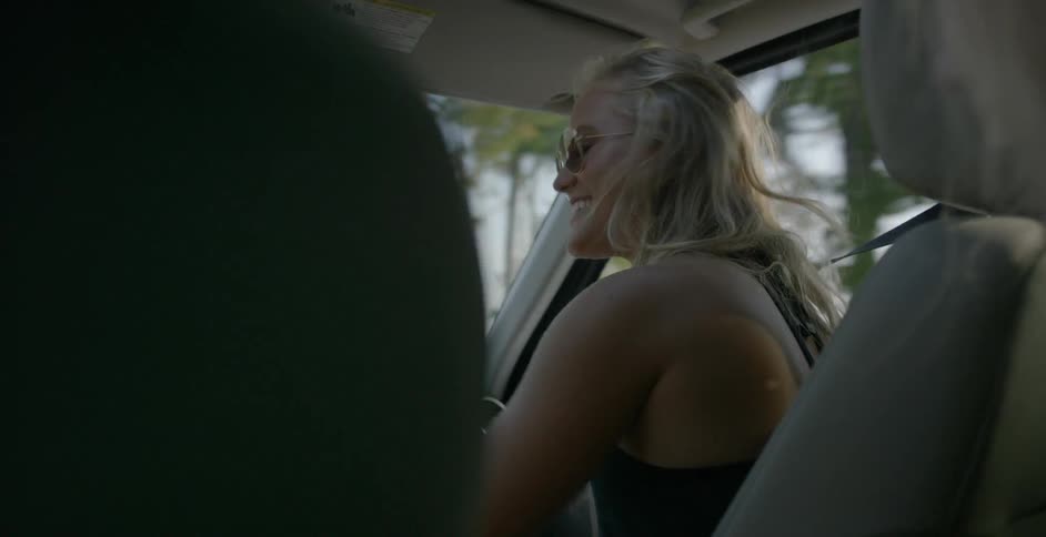 A woman sitting in the front seat of a car laughs at someone in the back seat