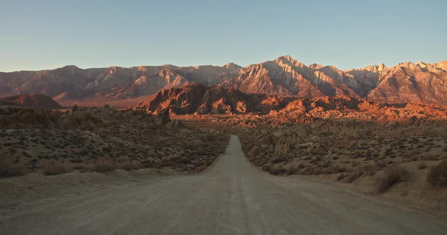 A road through the desert leads to mountains under a clear blue sky