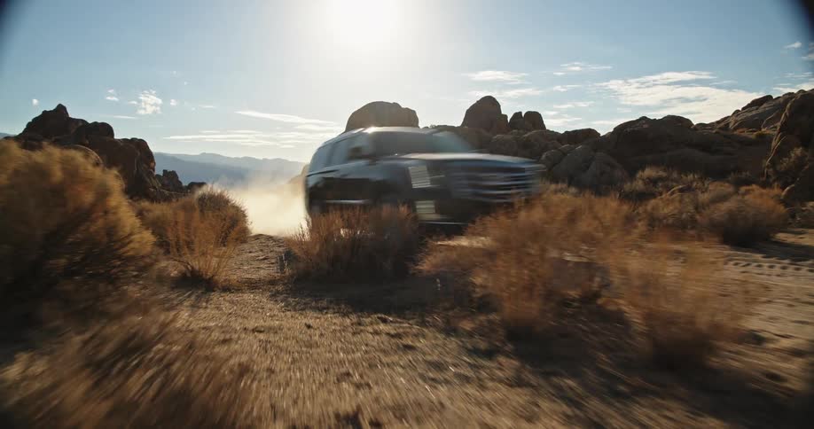 A vehicles leaves a cloud of dust behind it as it travels along a dirt road through the badlands during the day