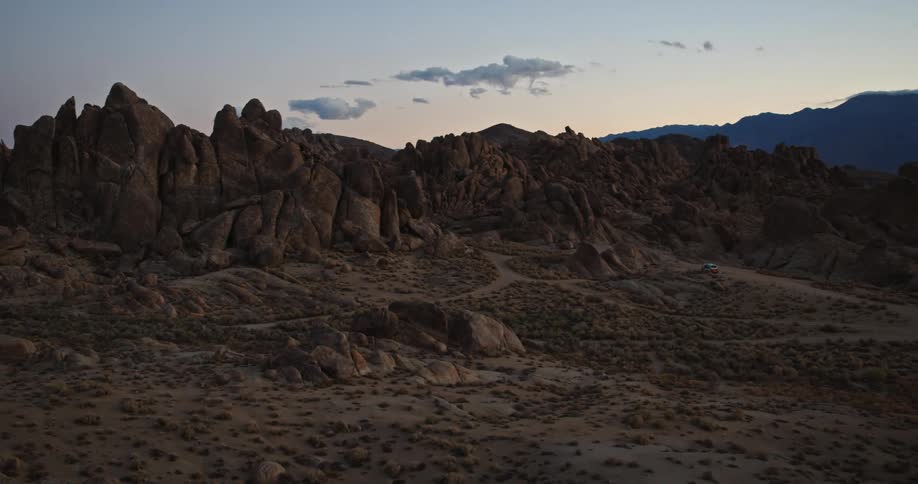 An automobile is parked on a dirt road near a mountain in the desert badlands