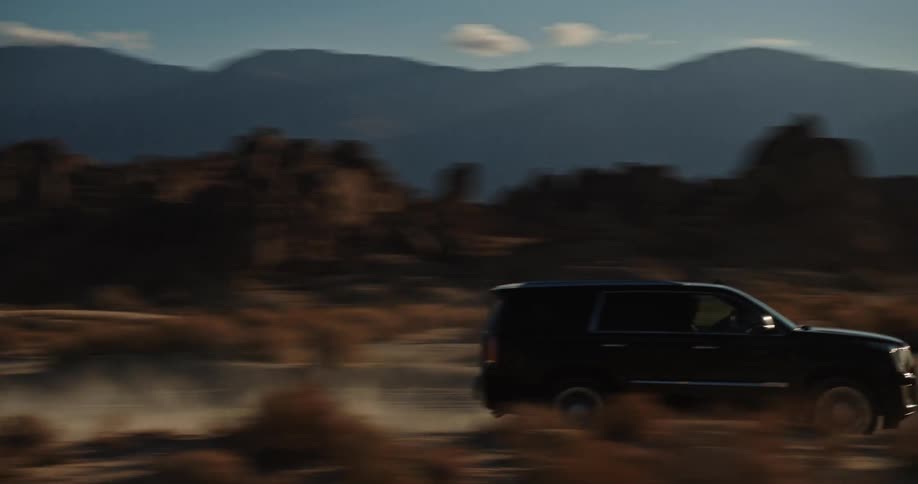 A black truck is traveling on a dirt road through the desert badlands and leaving a trail of smoke behind as it goes