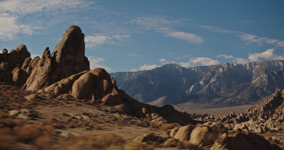 Rock outcroppings and rocky hills fill arid scrub land near wall of mountains