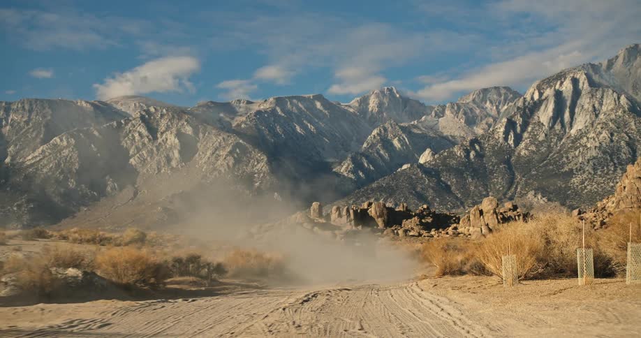 A vehicle travels along a dirt road through the badlands during the day
