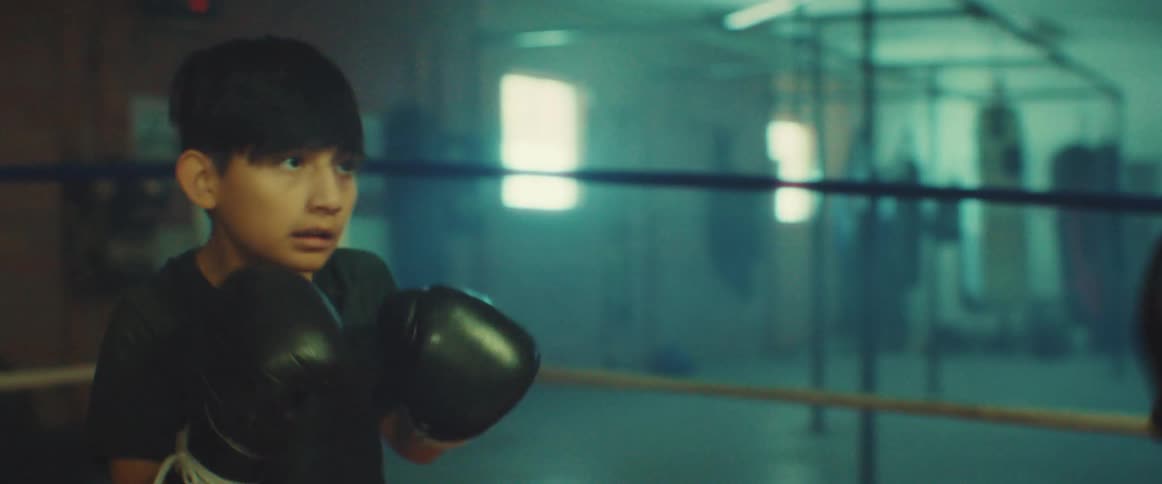 A young kid is boxing with an older man inside of a gym
