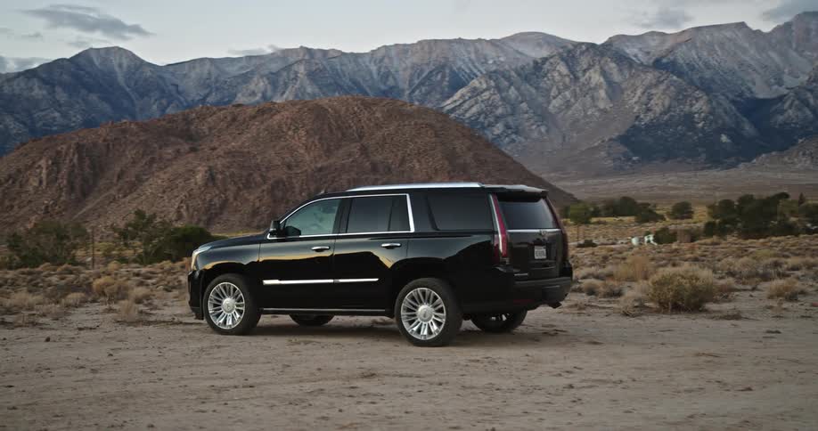 A black truck is parked on a desert mountain road under a cloudy sky