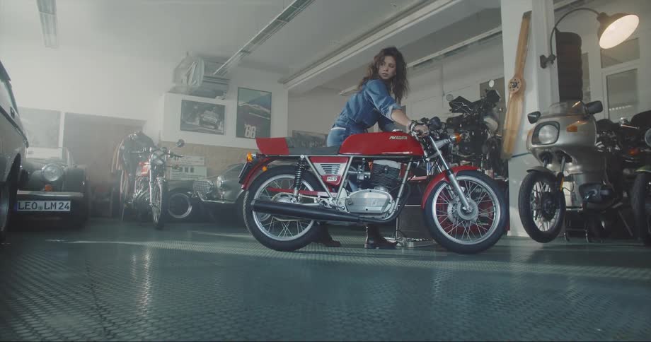 A woman pushes a motorcycle forwards and then backwards in a garage