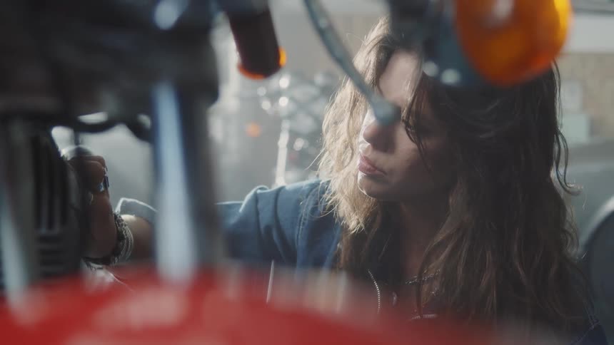 A female mechanic cleans the engine of a motorcycle in a garage during the day