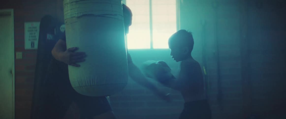 A young kid is boxing with another person in the middle of the day