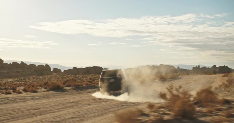Suv drives from smaller dirt road onto larger dirt road in arid area surrounded by mountains