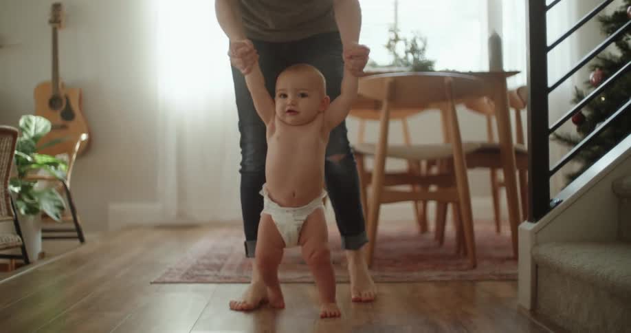 Mother holding the hands of her baby learning to walk at home
