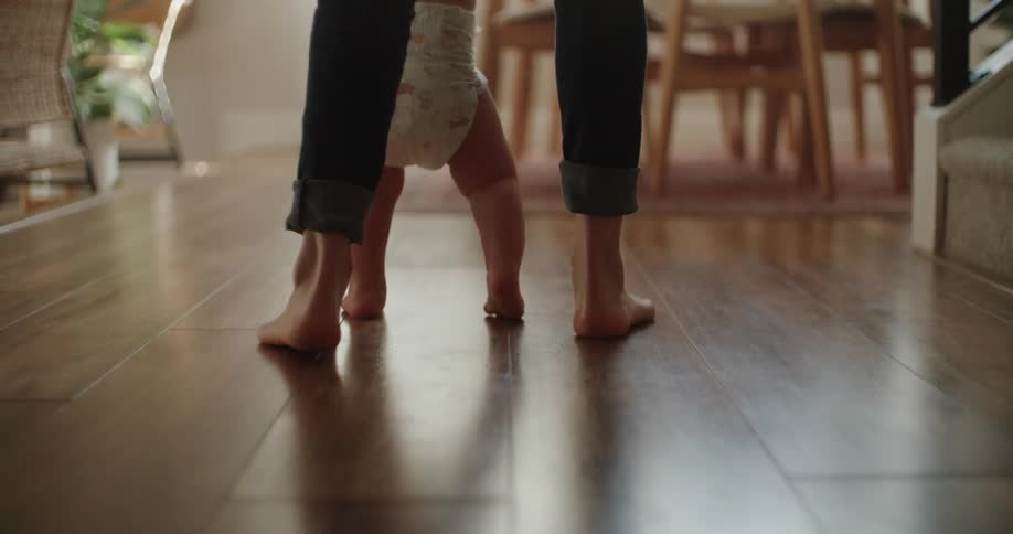 Mother teaching her infant son how to walk on the living room at home