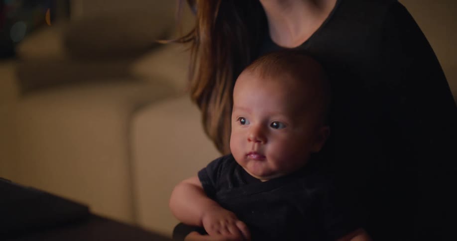 A woman uses a laptop while holding a baby in her lap