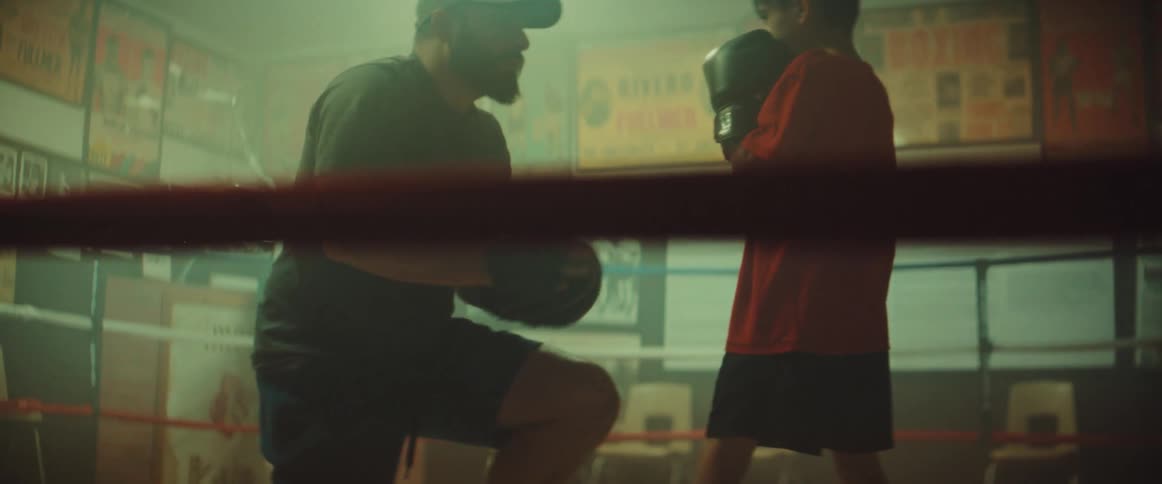 A boxing trainer helps a boy to adjust his boxing stance in a gym