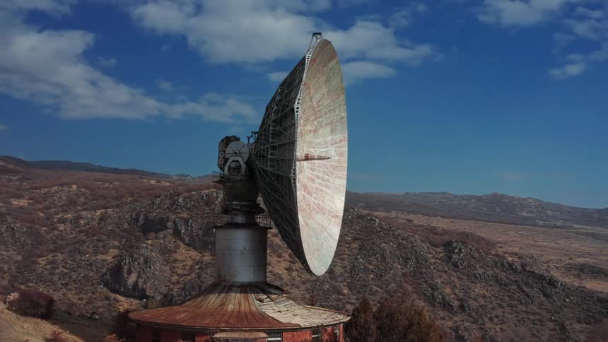Rusty radio telescope sits on building on mountain overlooking town