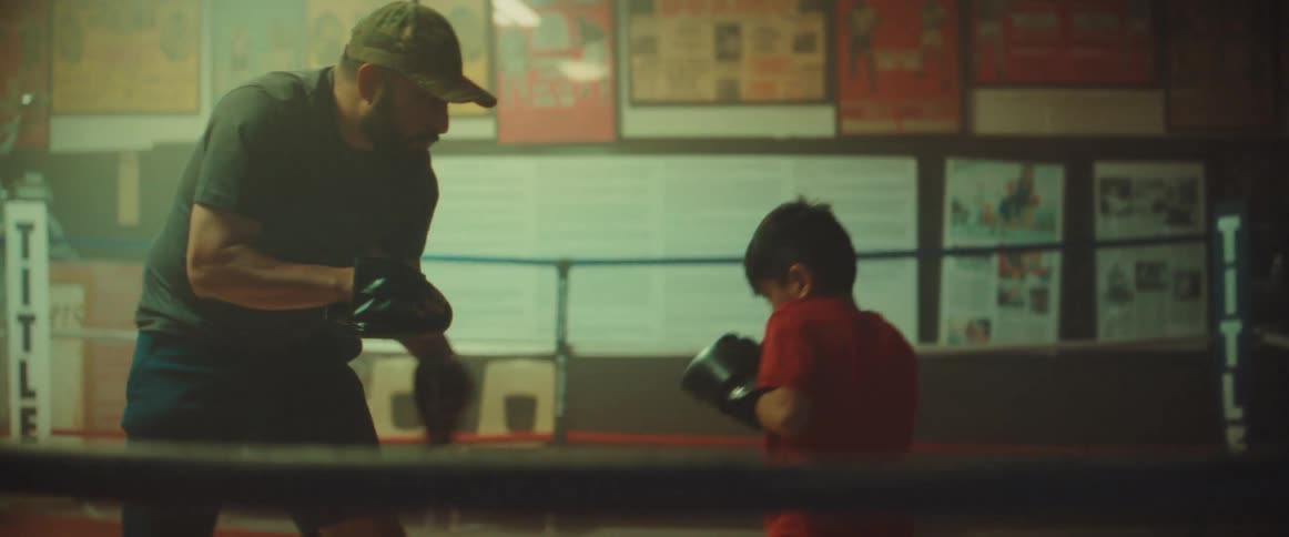 Man trains boy in boxing ring in dimly lit boxing gym
